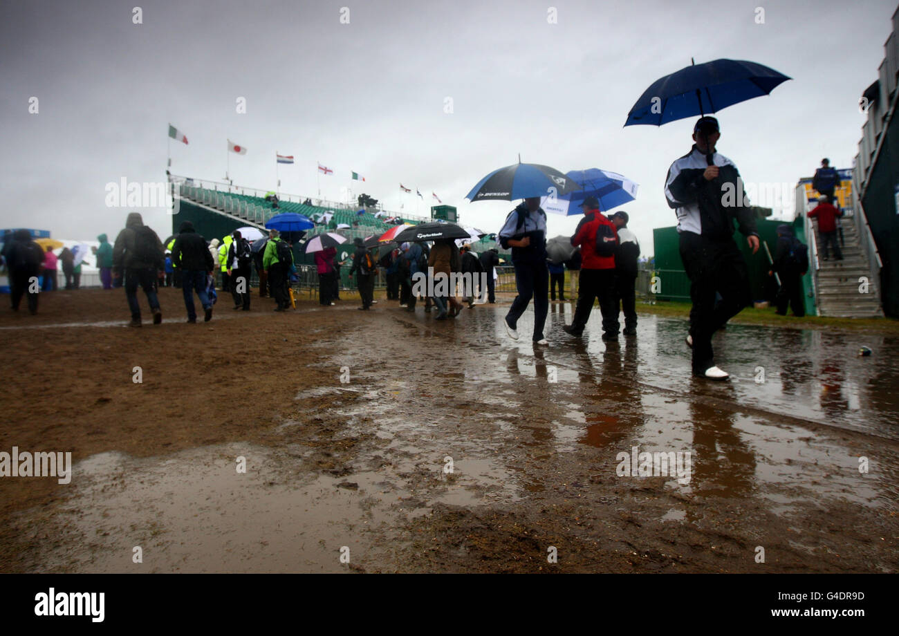 Spectators avoid puddles and mud as they make their way past the 18th green grandstand to shelter from the rain during round three of the 2011 Open Championship at Royal St George's, Sandwich. Stock Photo