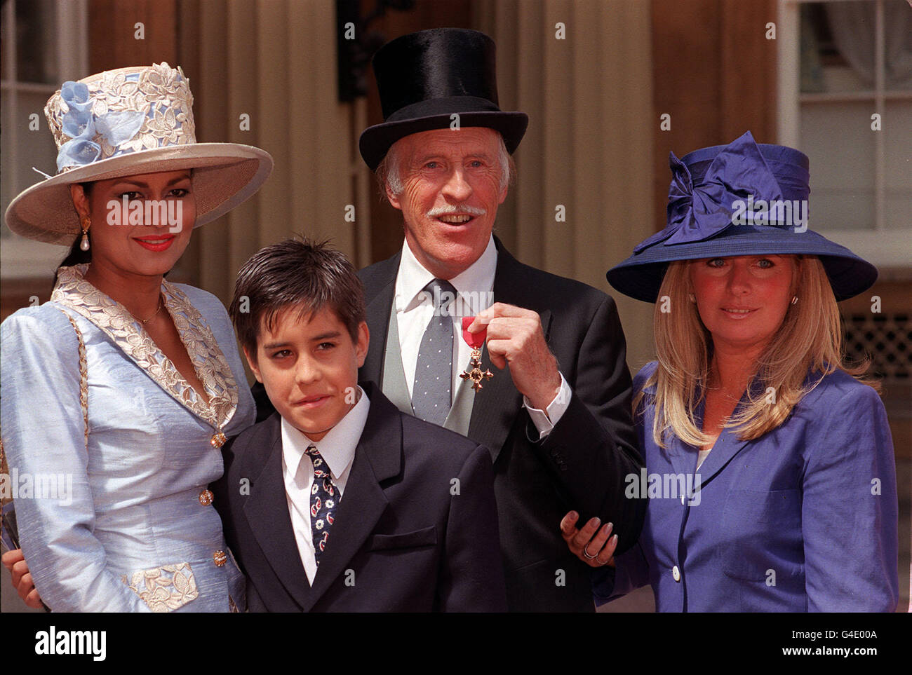 PA NEWS 22/7/98 ENTERTAINER BRUCE FORSYTH, WITH WIFE WILNELIA (LEFT) AND THEIR SON JJ, AND HIS DAUGHTER DEBBIE FROM HIS PREVIOUS MARRIAGE TO ANTHEA REDFERN, PROUDLY DISPLAYING HIS OBE WHICH HE RECEIVED FROM THE QUEEN DURING THE INVESTITURE CEREMONY AT BUCKINGHAM PALACE IN LONDON. Stock Photo