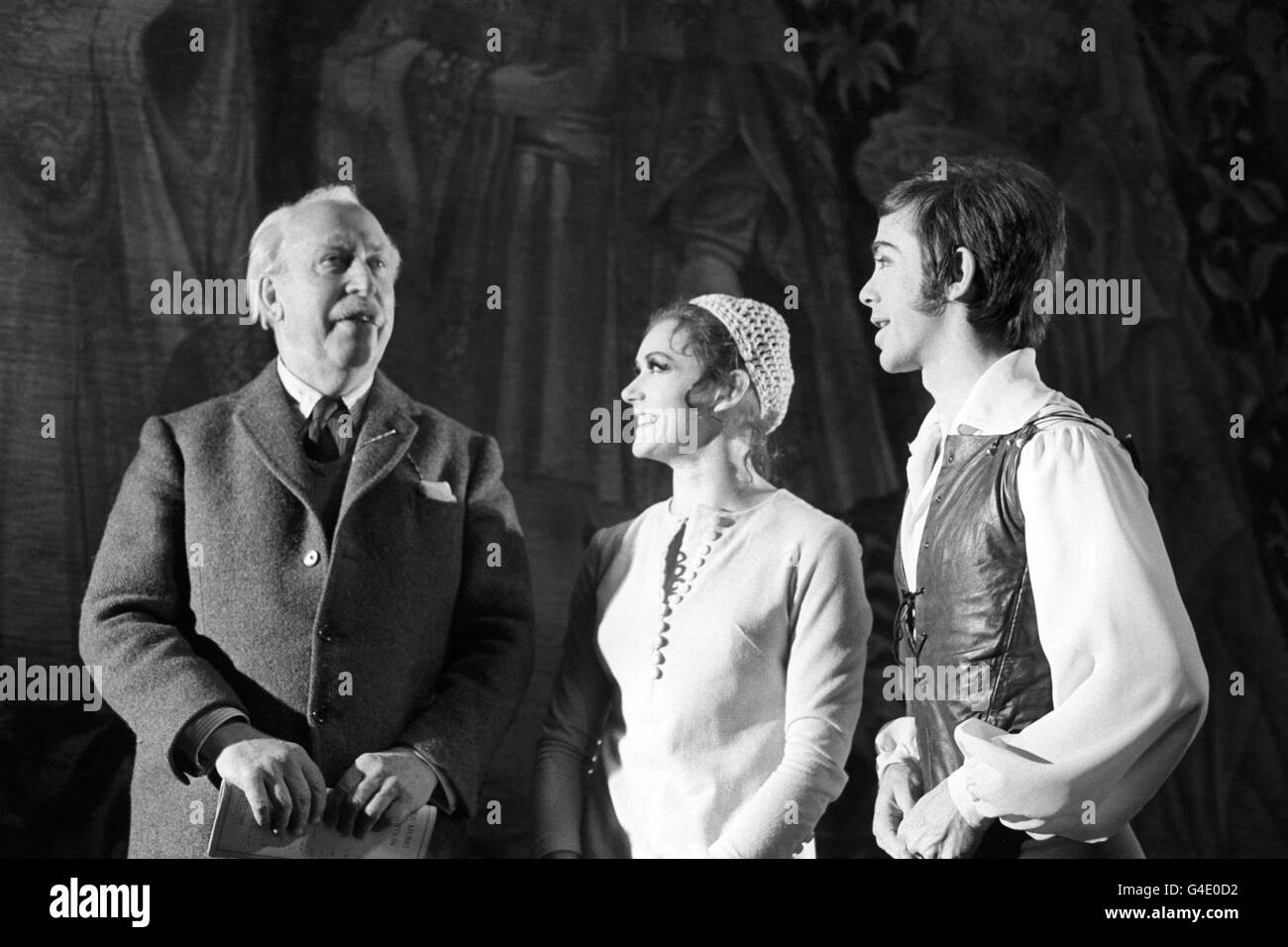 Seen on stage at the Sadler's Wells Theatre, Rosebery Avenue, London during rehearsals for 'Frontier' are the composer of the work, Sir Arthur Bliss (l), The Master of the Queen's Musick, and Scottish Theatre Ballet dancers Elaine McDonald (c) and Kenn Wells (r). Choreography and designs are by American John Neumeier (not pictured). The story of 'Frontier' figures in a tapestry (seen in the background) which comes to life. The original tapestry is in the Musee de Cluny, Paris. This was to be the the Scottish Ballet's first London season since changing their name from Western Theatre Ballet. Stock Photo