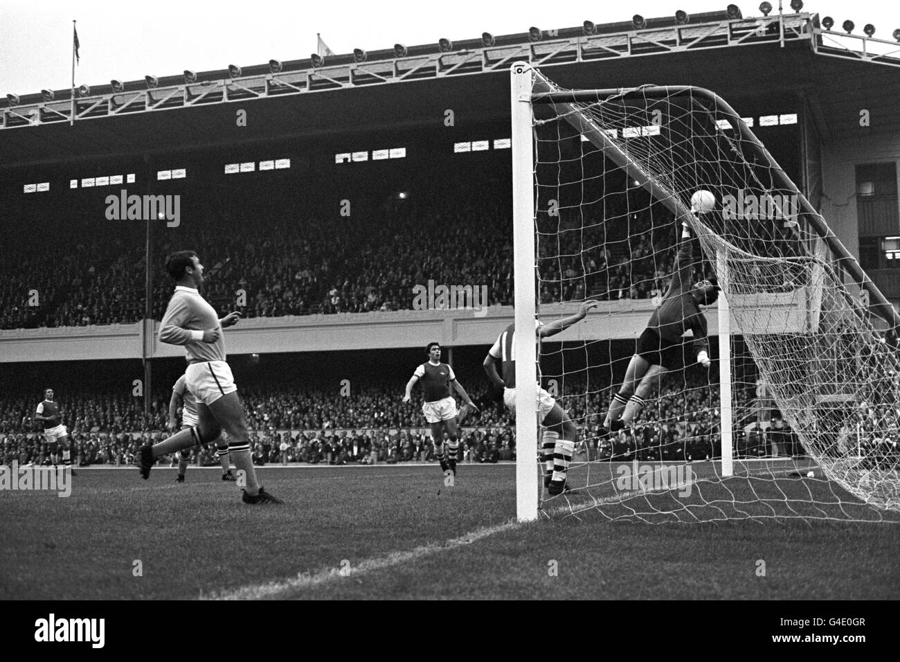 Manchester City goalkeeper Ken Mulhearn tips the ball over the cross bar to save from Arsenal's Bobby Gould (c). Arsenal's David Jenkins (behind goalpost) in following up along with Manchester City's Glyn Pardoe (l). Stock Photo