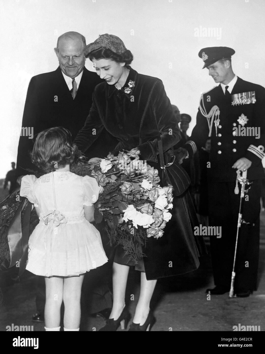 Princess Elizabeth receives flowers from a little girl, on arrival in Toronto, Canada. In the background, right, is the Duke of Edinburgh Stock Photo