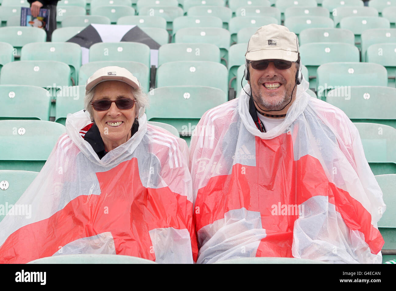 Fans sit in the stands covered in an England Poncho sheltering from the rain during the First Natwest One Day International at the Kia Oval, London. Stock Photo