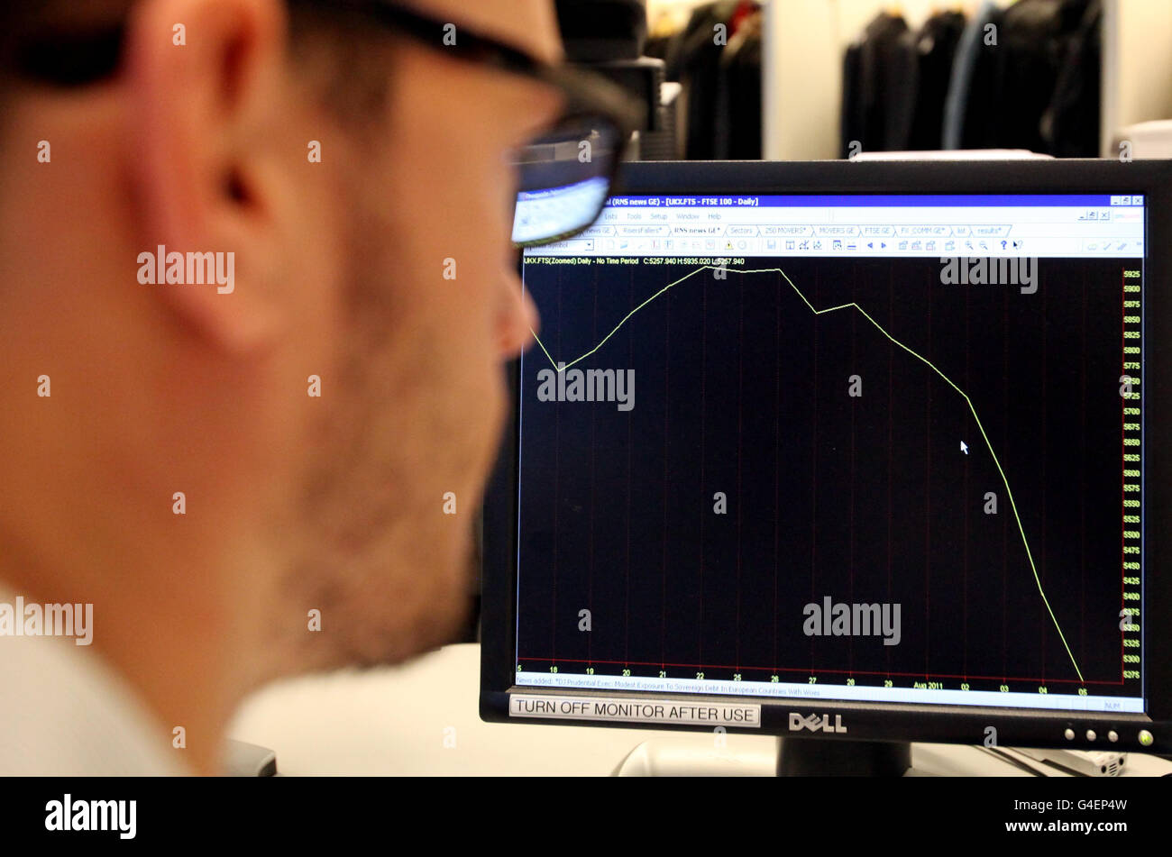 A worker looks at graph showing the FTSE 100 index from mid July to August 5th as London's leading shares index sustained more heavy losses today as the turmoil engulfing world markets showed no signs of easing. Stock Photo