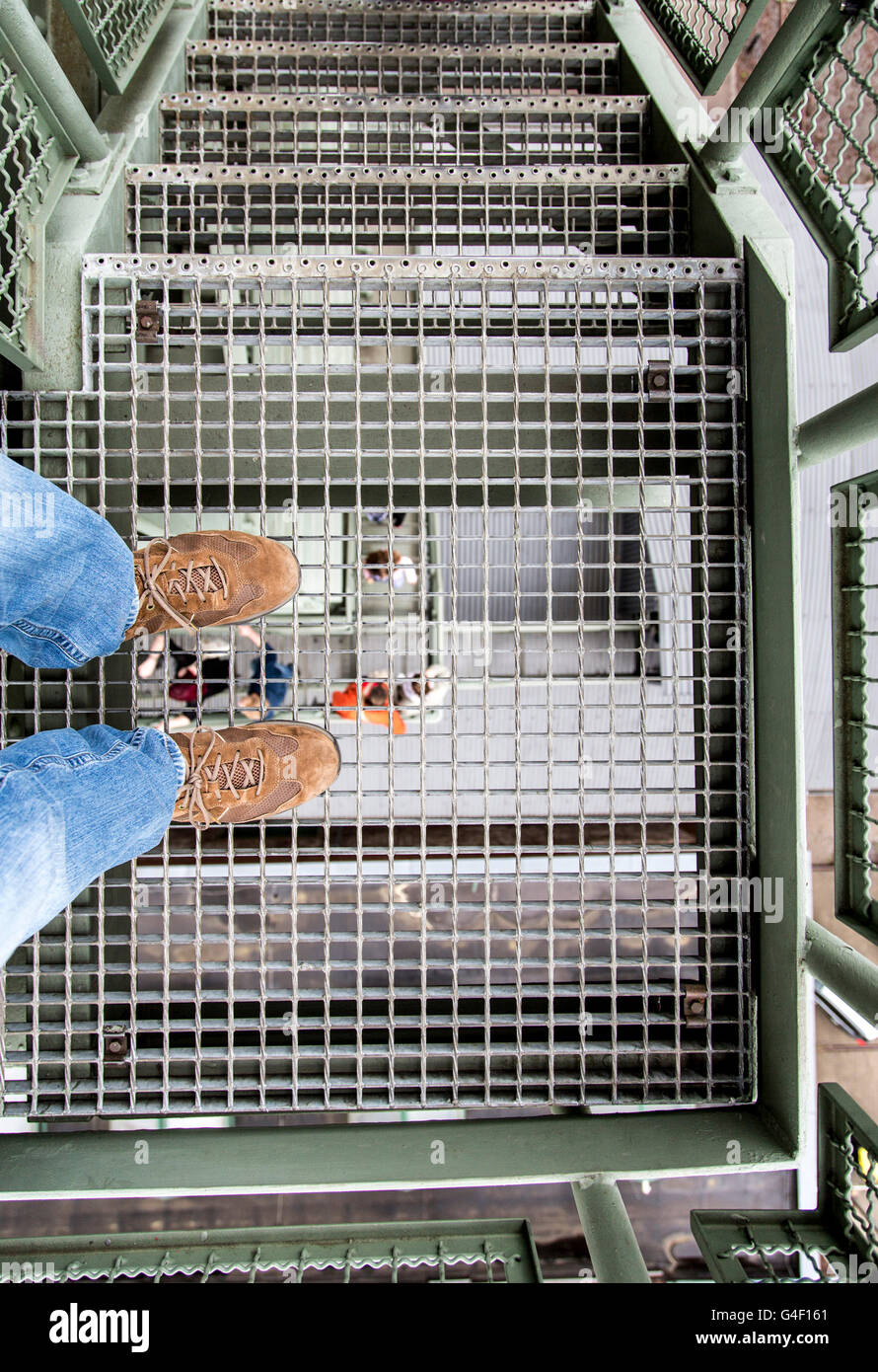 Symbol picture about acrophobia, person stands on the metal grid of a staircase, looking down into the depths, Stock Photo