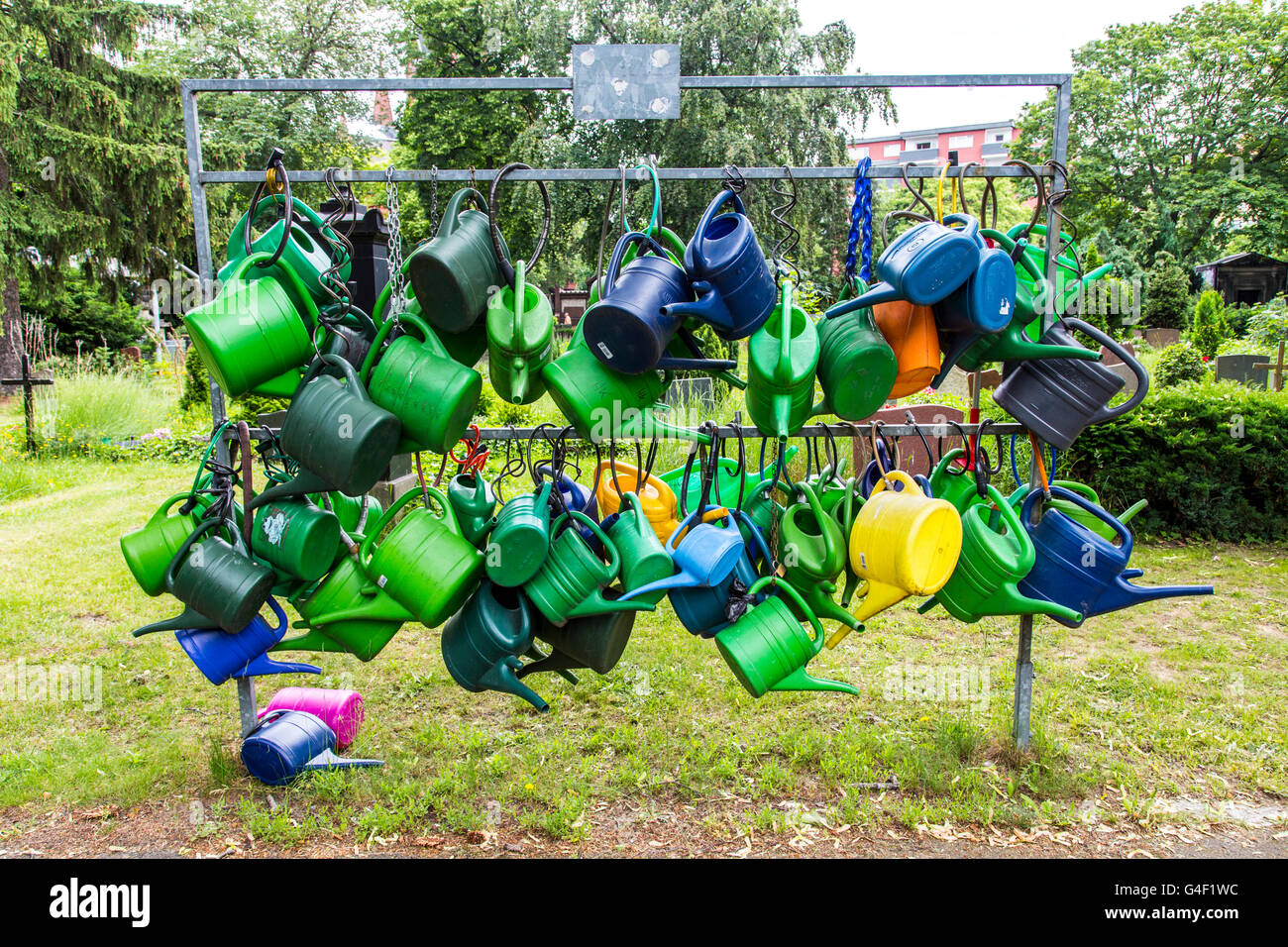 Many plastic watering cans hanging on a rack, secured with bicycle locks, anti-theft, in a cemetery, Stock Photo