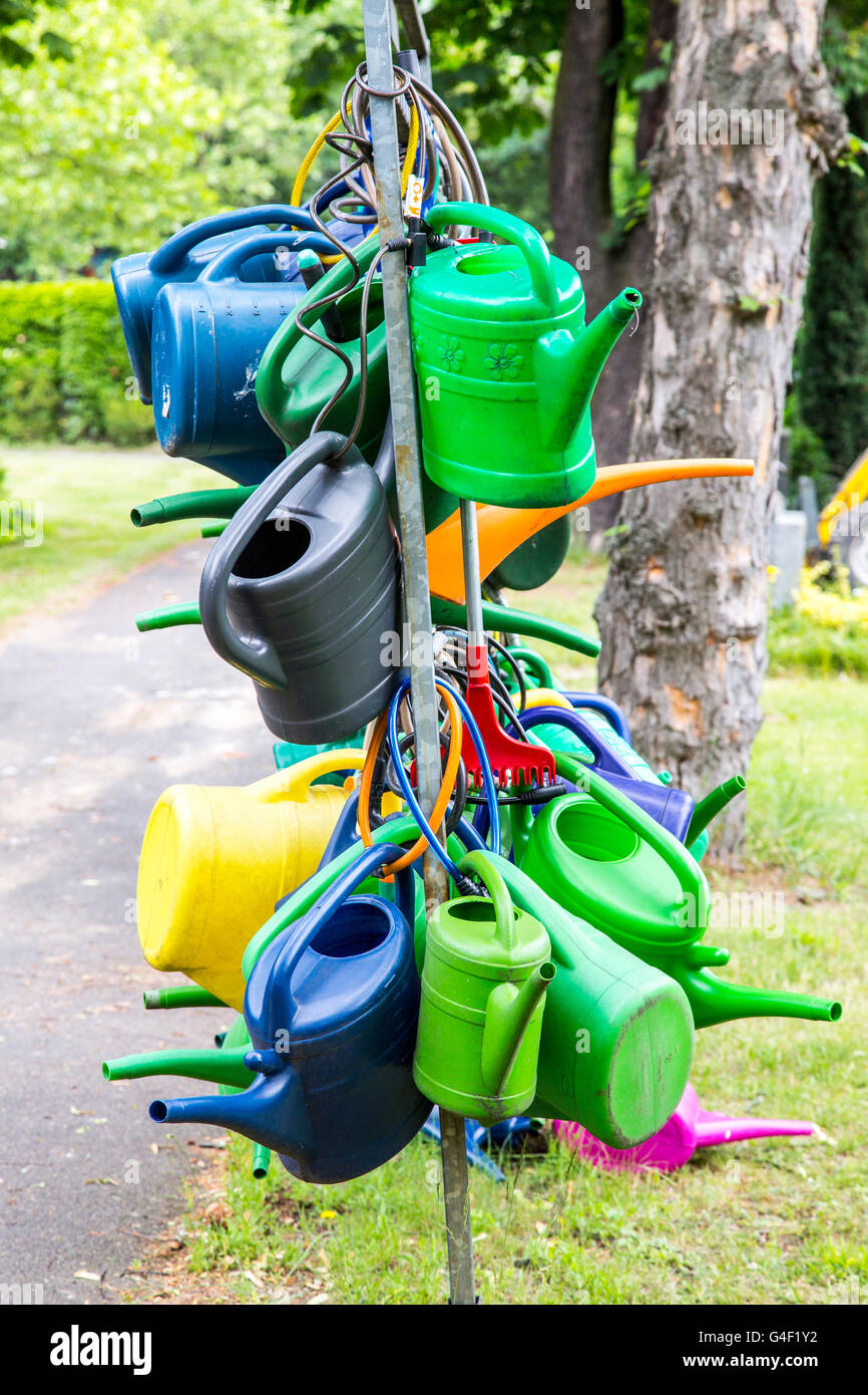 Many plastic watering cans hanging on a rack, secured with bicycle locks, anti-theft, in a cemetery, Stock Photo