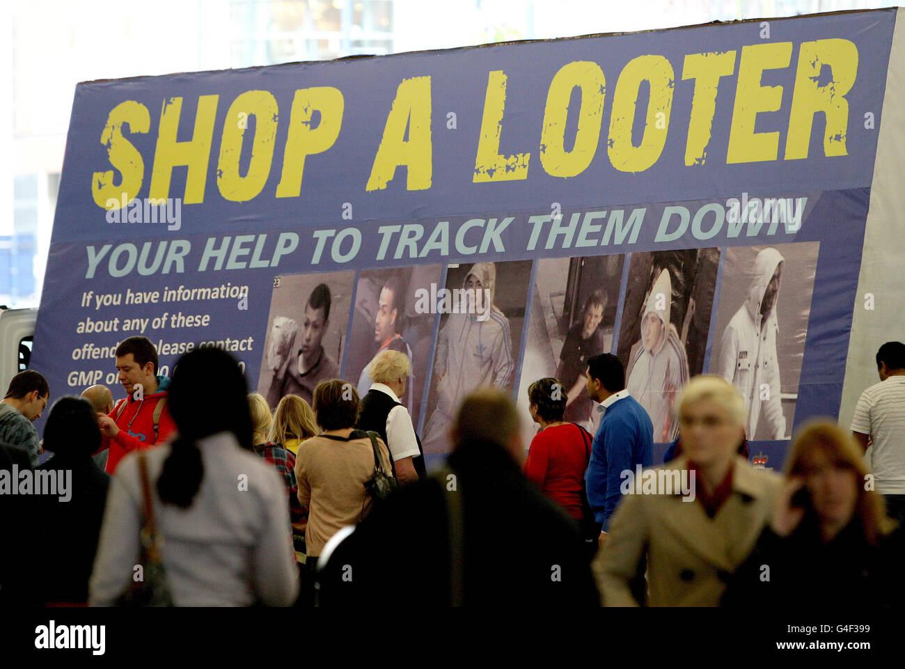 Shoppers walk past a Greater Manchester Police 'Shop A Looter' board on Market street in Manchester city centre. Stock Photo