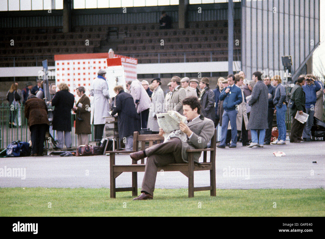 Horse Racing - January Races - Kempton Park Racecourse. A racegoer users his newspaper to look up the latest odds as punters queue to place bets in the background Stock Photo