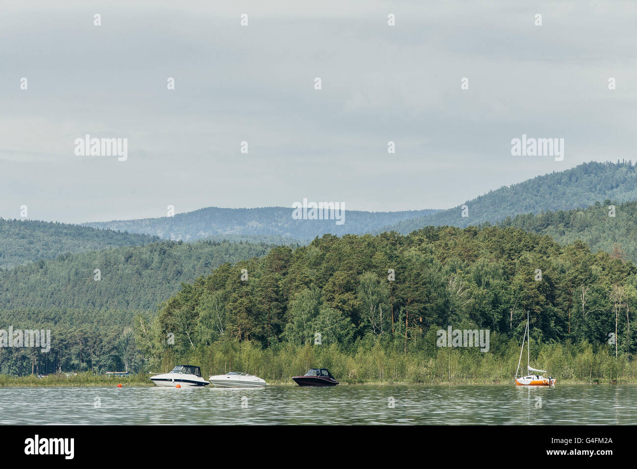 motor boats and yacht stand at shore of lake on background of mountains and forest Stock Photo