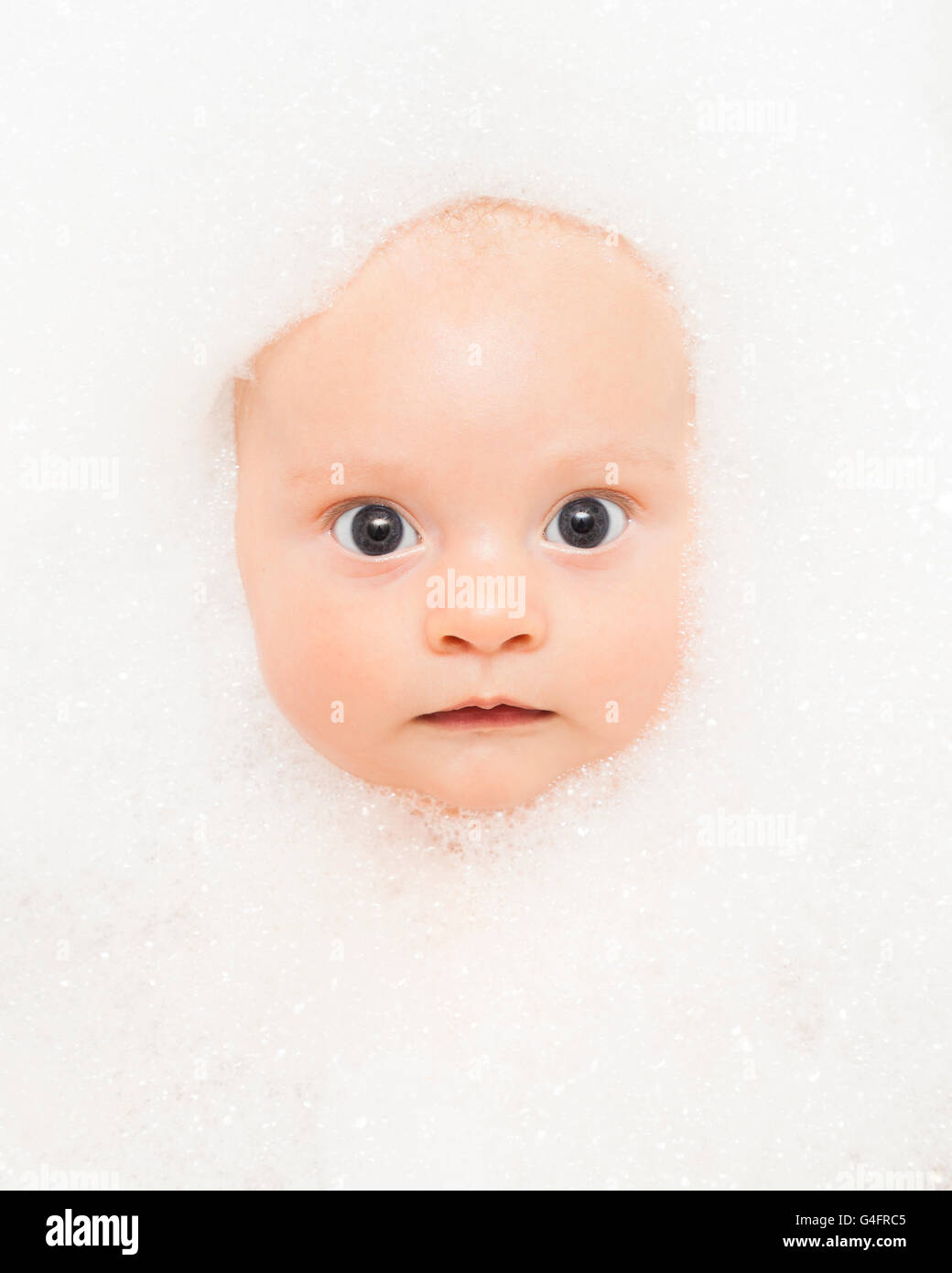 Three month old baby boy in the bath. His face surrounded by bubbles