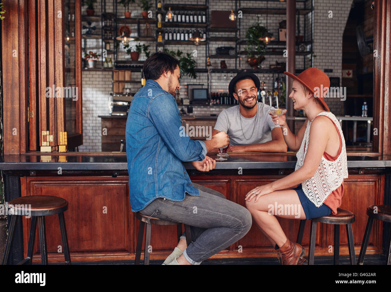 Portrait of three young friends smiling and sitting in a cafe having drinks together. Young men and woman meeting in a coffee sh Stock Photo