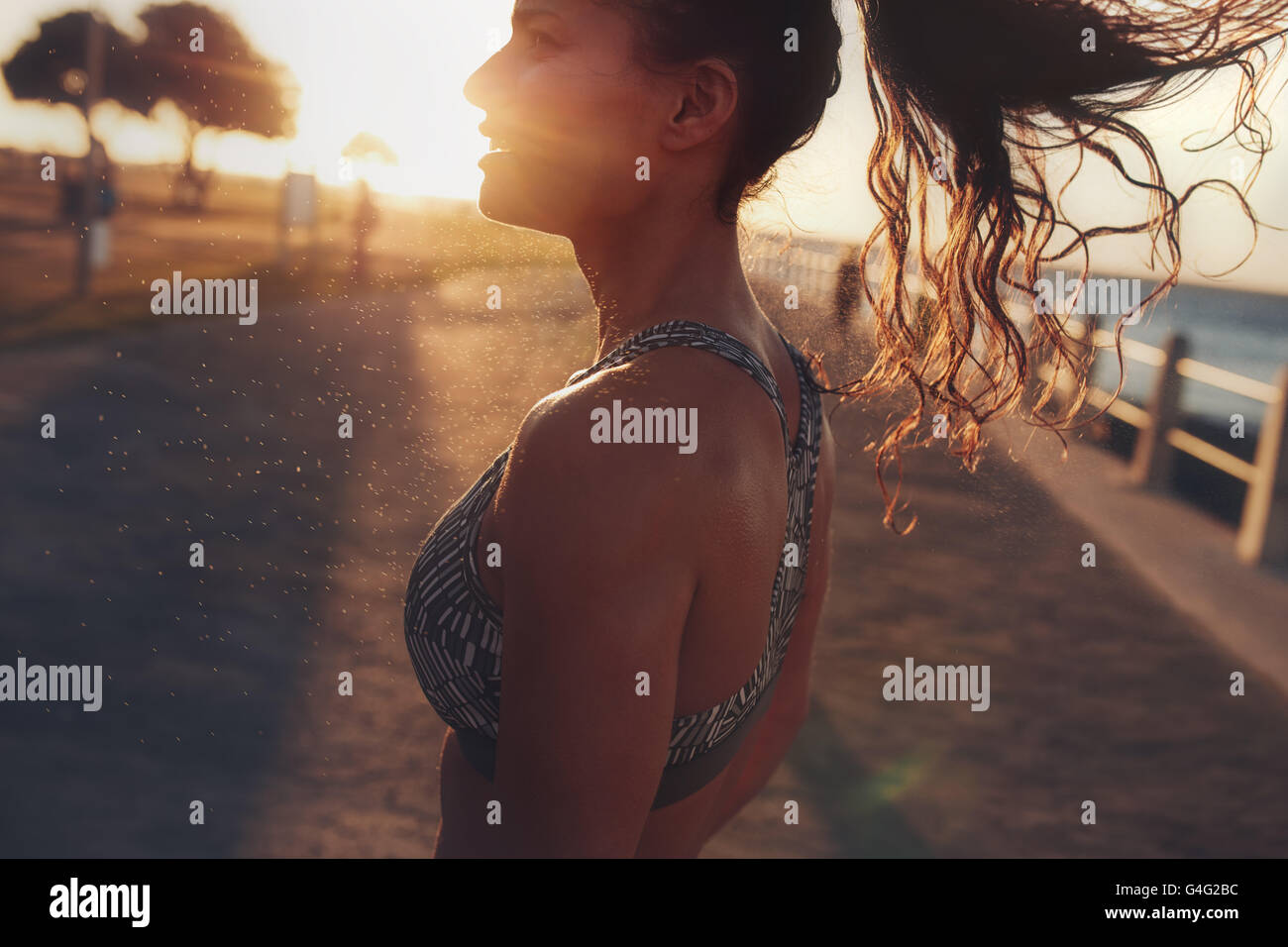 Close up image of fitness woman standing outdoors during evening. She is relaxing after her workout session, with bright sunligh Stock Photo