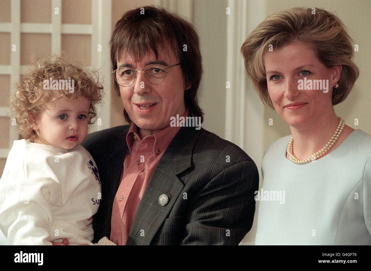 SOPHIE RHYS-JONES POSES WITH BILL WYMAN, A FORMER MEMBER OF THE BAND 'THE ROLLING STONES', AND HIS DAUGHTER KATHARINE AT THE LAUNCH OF NATIONAL MOTHER AND BABY WEEK IN AID OF BABY LIFELINE. * 18/9/2000: Channel 4 was rapped for screening a spoof interview with Wyman without the star's permission. The musician complained to the Independent Television Commission after he was duped into appearing in the chat sequence which was used for the Candid Camera-style Trigger Happy TV show. The ITC upheld the complaint and said the station had broken programme rules 'by its failure to secure permission Stock Photo