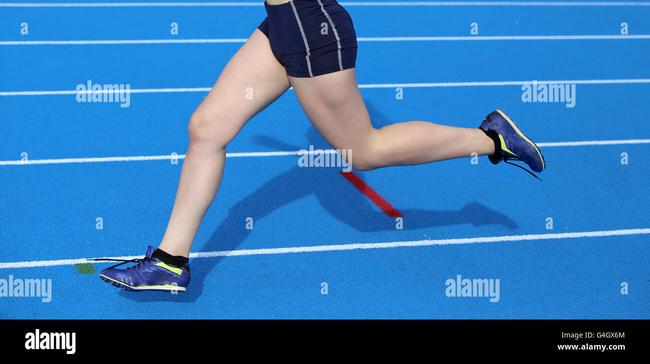 young woman running on the athletics track with blue colored lanes Stock Photo
