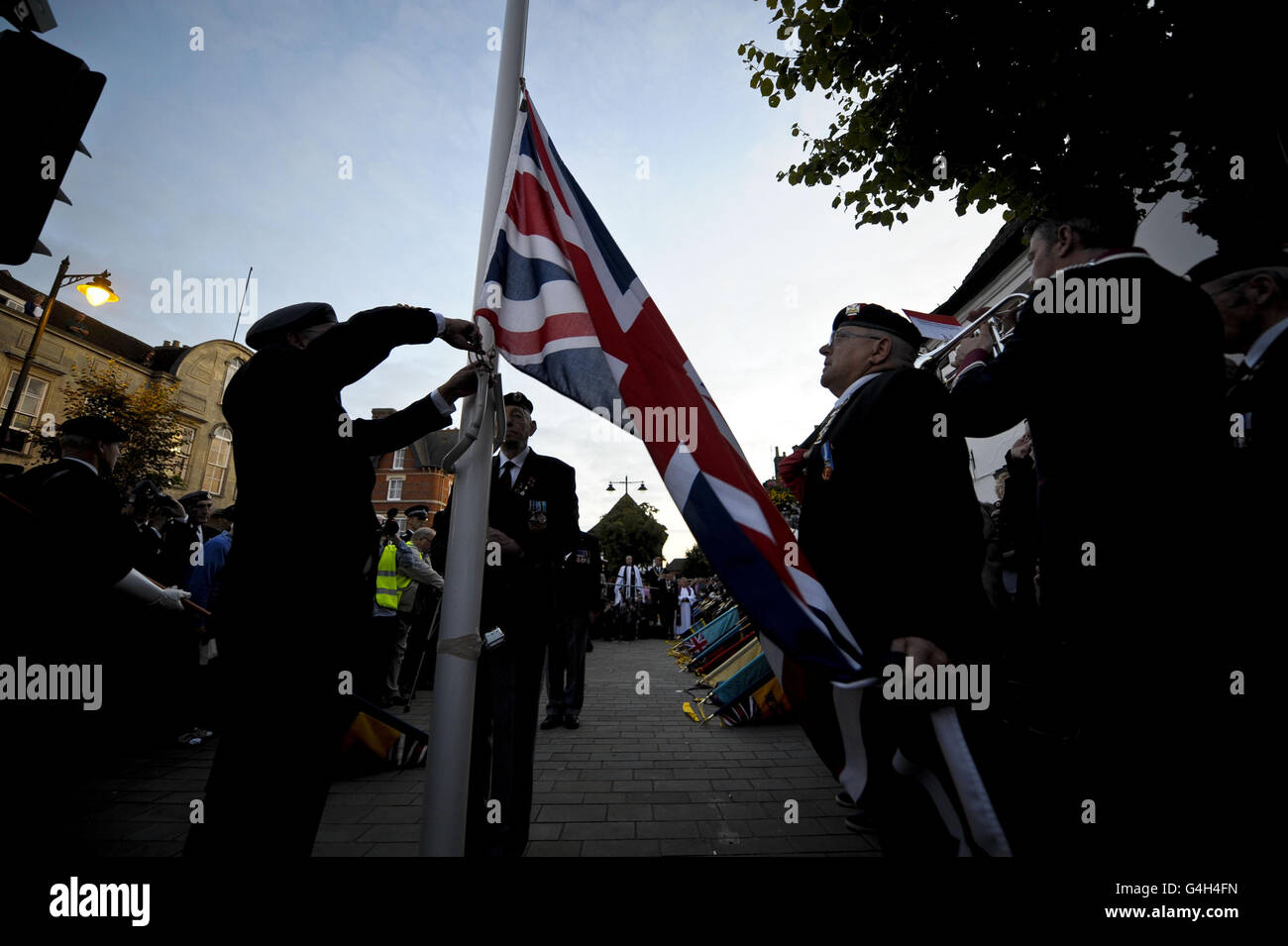 The official flag party stand beneath the Union flag as it is lowered for the last time on the High Street of Wootton Bassett as they hand over the ceremonial flag to Oxford where the bodies of fallen servicemen will now be repatriated into the UK at RAF Brize Norton. Stock Photo