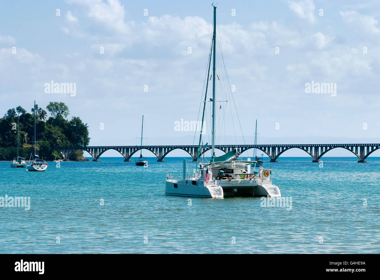 View of a catamaran and sail boats ancored at Samana Bay and  Los Puentes bridge at the background, Samana, Dominican Republic. Stock Photo