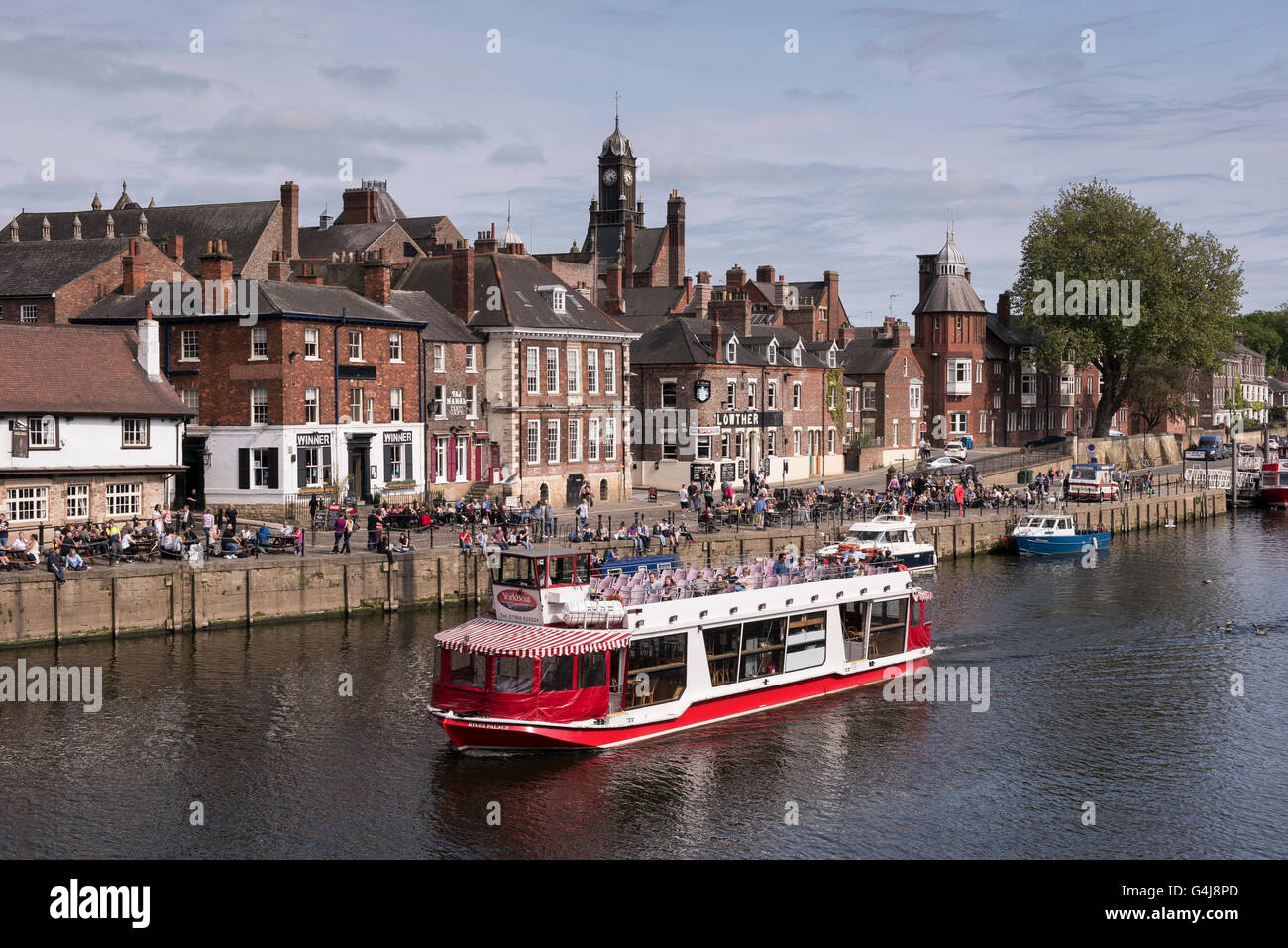 City Cruises boat sailing on sunny scenic River Ouse past people sitting relaxing outside riverside pubs & restaurants - York, Yorkshire, England, UK. Stock Photo