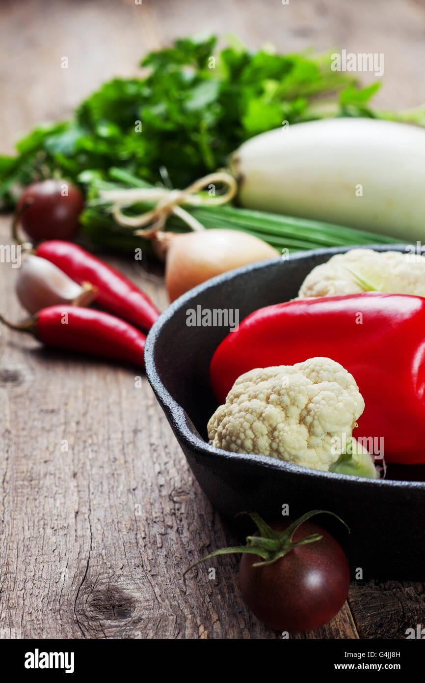 cast iron pan and fresh vegetables for the preparation of healthy vegetarian food on wooden