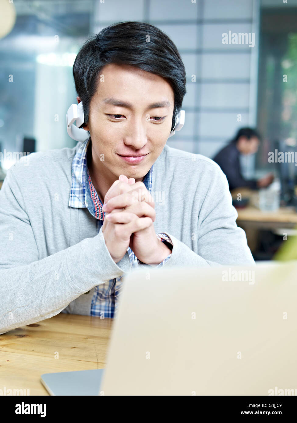 young asian business person looking at laptop computer with listening to music with headphones in office. Stock Photo
