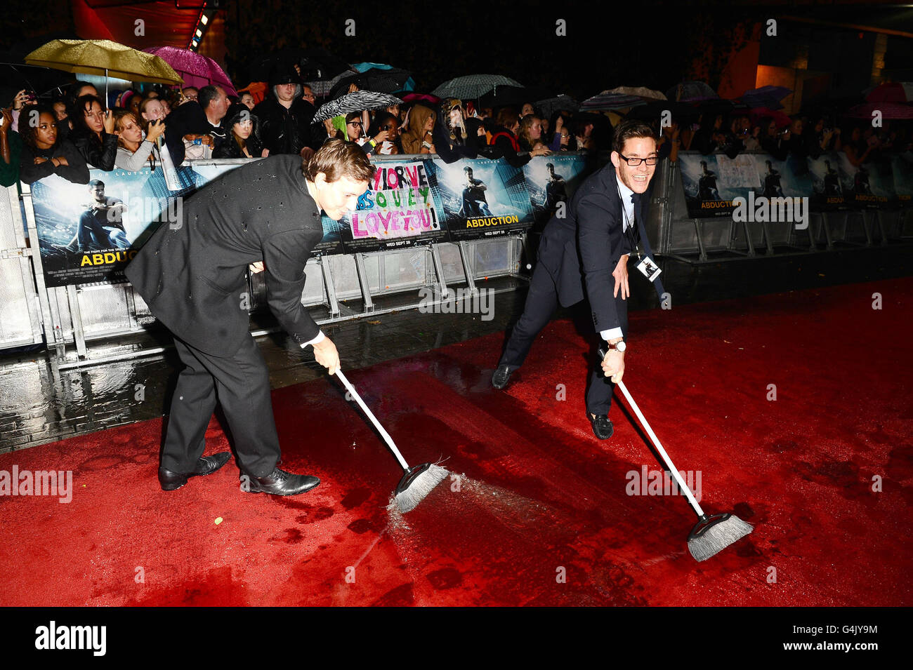 Rain water is swept off the red carpet before the premiere of new film Abduction at the IMAX cinema in London. Stock Photo