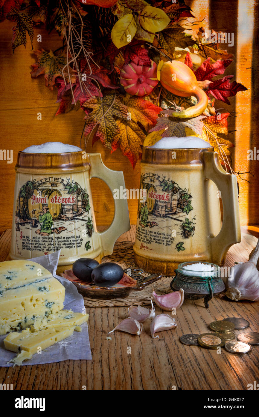 Still life of two mugs beer, with a praying monk in the picture, and Roquefort cheese appetizer, two black olives. 20 x 13 x 0.1 Stock Photo