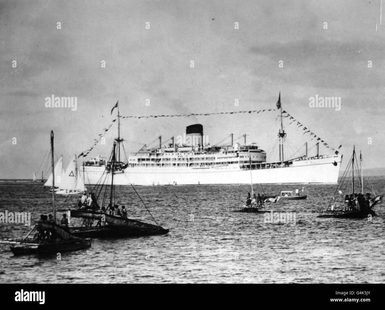 Native war boats (in foreground) welcome the liner Gothic, in which the Queen and the Duke of Edinburgh are voyaging on their Commonwealth tour, as it enters the reef at Suva, Fiji. Stock Photo