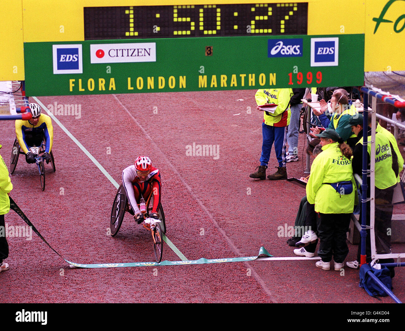 Swiss competitor Heinz Frei crosses the finish line to win the 1999 London Marathon men's wheelchair race, as the readout above records his winning time. Stock Photo
