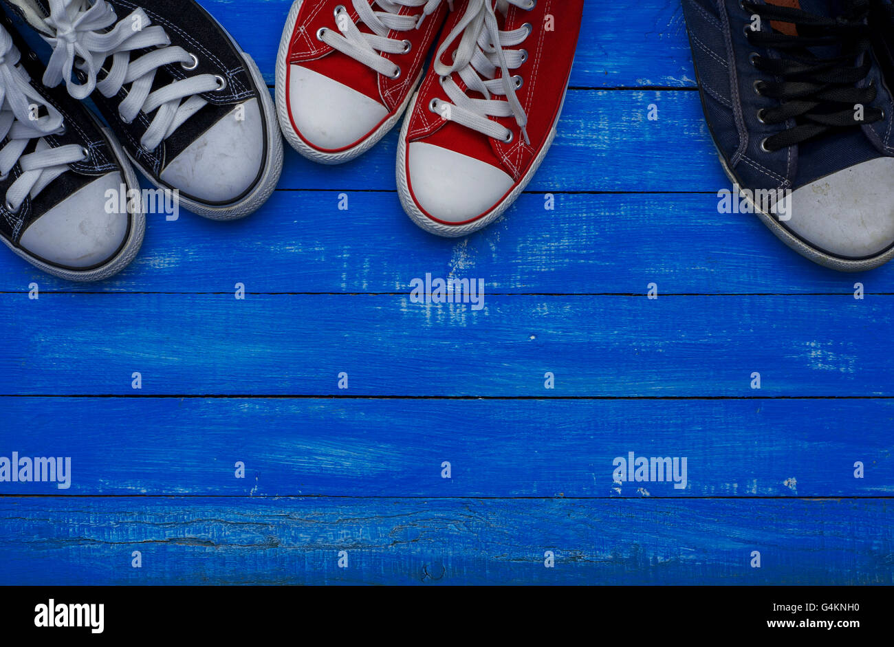Three pairs of sneakers of different sizes on a blue vintage wooden floor Stock Photo