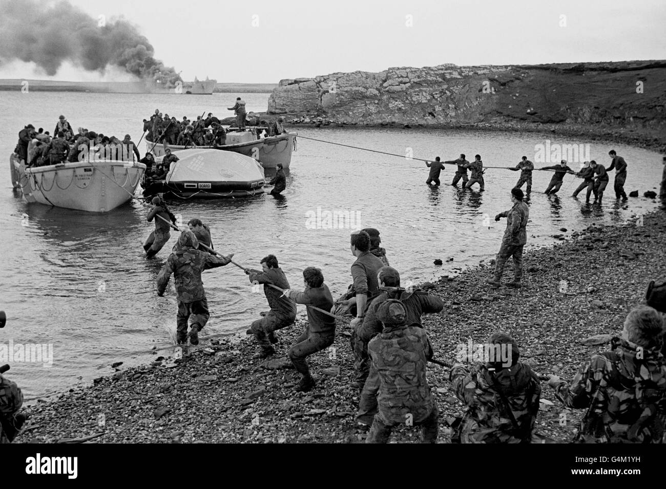 2ND APRIL: On this day in 1982 Argentina invaded the Falkland Islands. THE FALKLANDS WAR: RAF Sir Galahad (smoking in the background) survivors are hauled ashore by colleagues at Bluff Cove, East Falkland, after the Argentinian air attack during the Falklands conflict. The ship was eventually towed out to sea and sunk as a war grave. Stock Photo