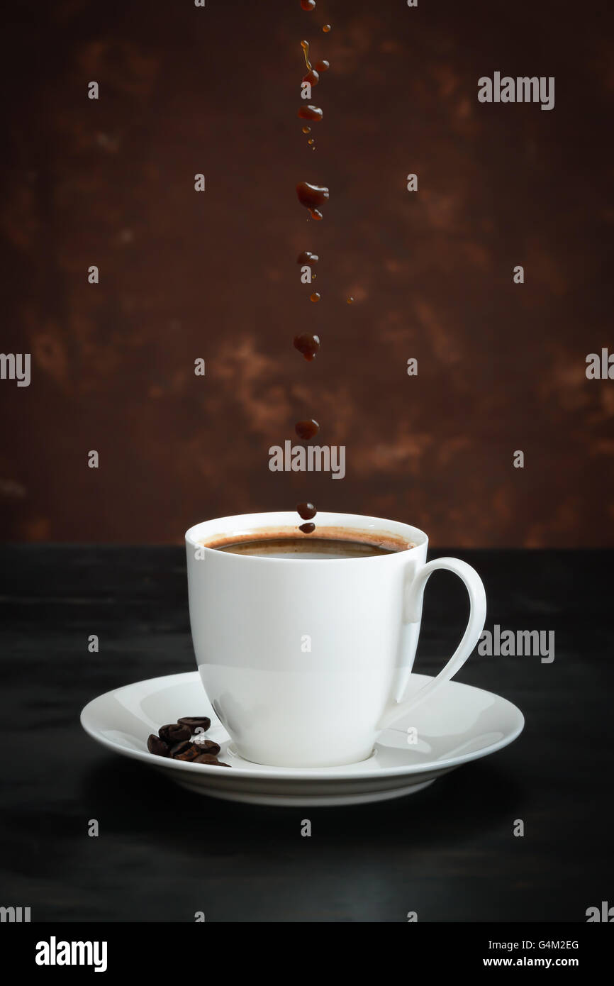 Coffee cup and beans with coffee drops on black wood background. Stock Photo