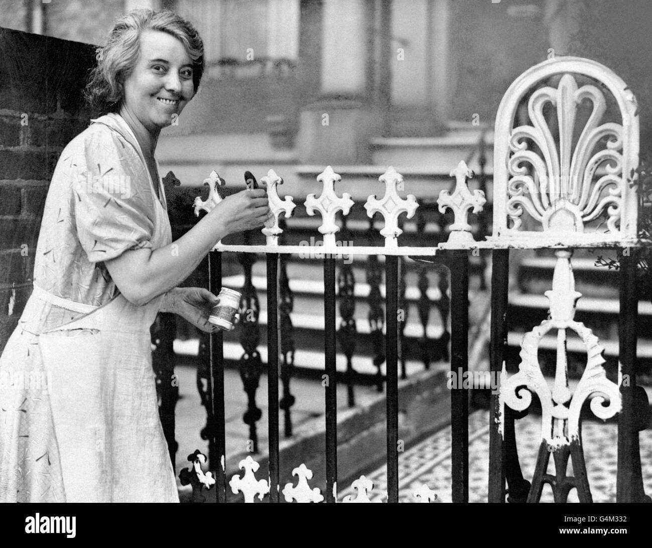 A woman paints her railings white in London, to make things easier during the blackout, during the Second World War. Stock Photo