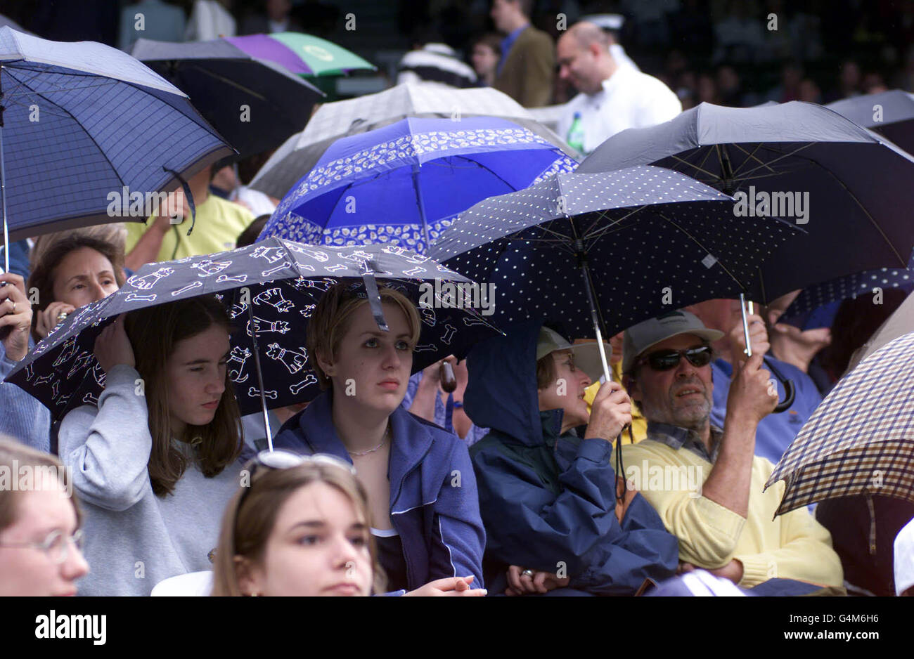 No Commercial Use: Tennis fans on Centre Court take cover under umbrella's as rain stops play during the Tim Henman v Jim Courier match at the Wimbledon Tennis Championships. Stock Photo