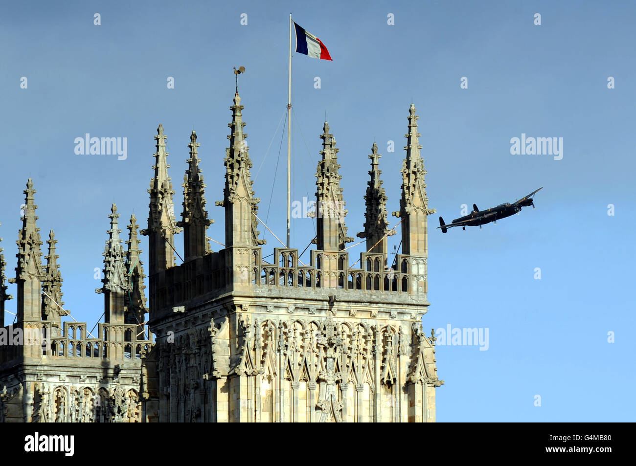 A French/Anglo flag is flown from York Minster as a Lancaster bomber from the Battle of Memorial Flight flies by during an Anglo/French flypast following a memorial service at York Minster, for the inauguration of a memorial stone commemorating the French airmen based in York, who fought with RAF Bomber Command in WWII. Stock Photo