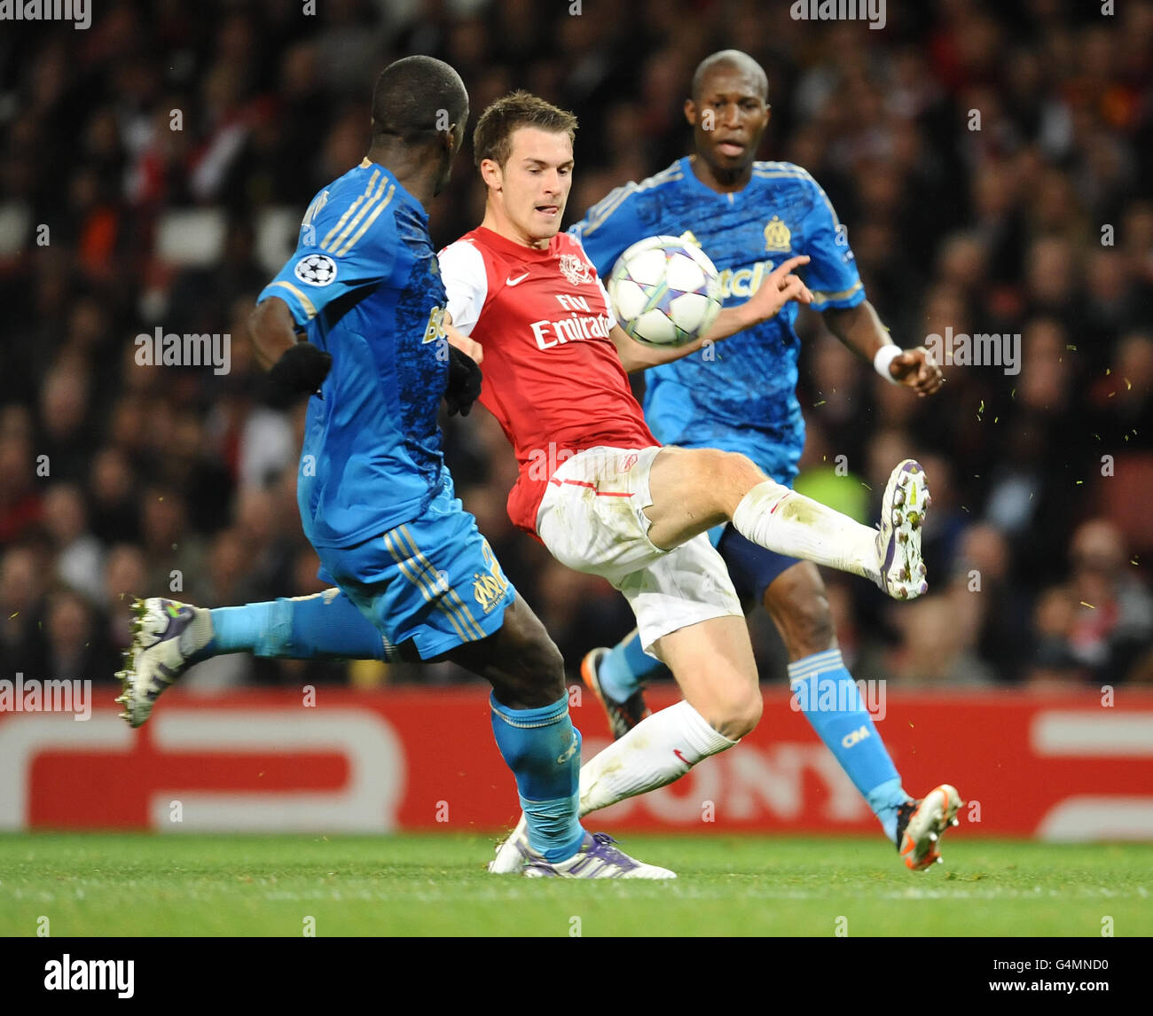 Arsenal's Aaron Ramsey (centre) is challenged by Olympique Marseille's Olympique Marseille's Souleymane Diawara (left) and Rod Fanni during a UEFA Champions League Group F match at the Emirates Stadium, London. Stock Photo