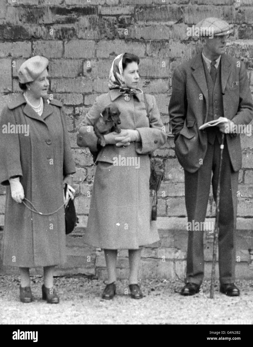 Queen Elizabeth II holds the Queen Mother's dachshund as, with their host the Duke of Beaufort, they watched horses taking part in the Badminton Horse Trials exercising in the stable yard. Stock Photo