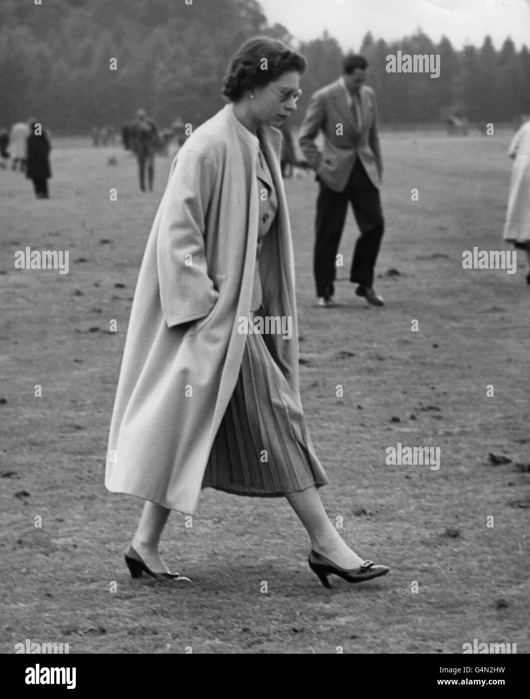 Queen Elizabeth II walks onto the field to tread down divots kicked up by the ponies during a polo match in which the Duke of Edinburgh was playing, at Windsor Great park. Stock Photo