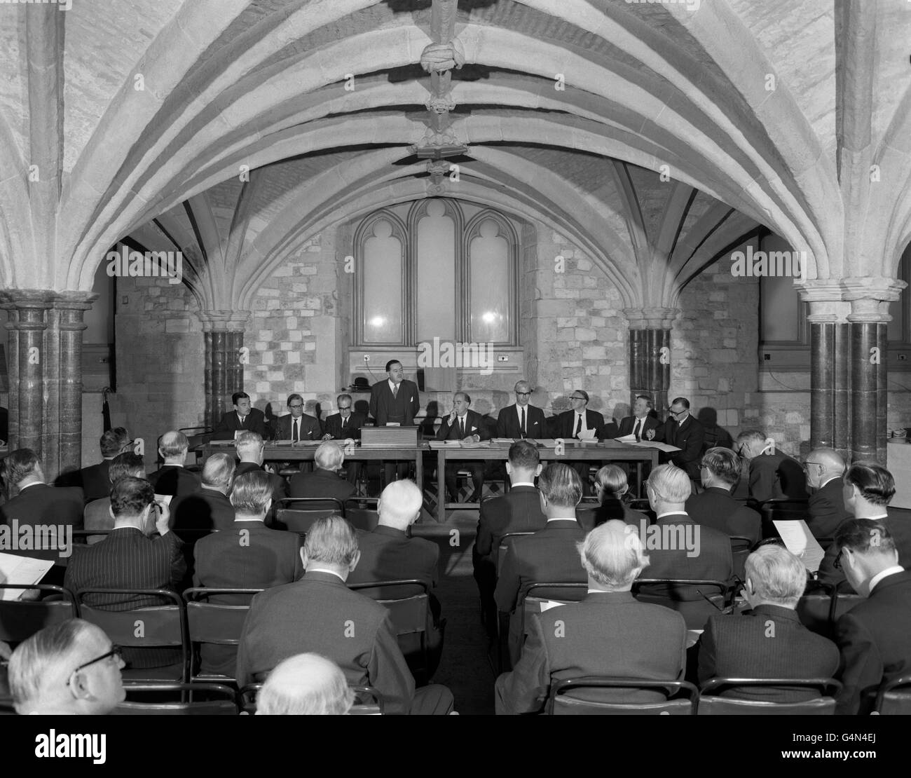 An historic setting, the Crypt beneath Guildhall, London, for the one hundredth annual general meeting of The Press Association, Britain's national news agency, which is celebrating it's centenary. The Chairman of the PA, Mr W D Barnetson (Chairman and Joint Managing Director, United Newspapers Ltd.), is seen addressing the meeting. Seated at the tables are directors and two of the officers of the Association. (l-r) L. J. Stallard (Joint Managing Director and General Manager, the Midland News Association Ltd), the Vice-Chairman, A. M Burnett-Stuart (Joint Deputy Managing Director, Thomson Stock Photo