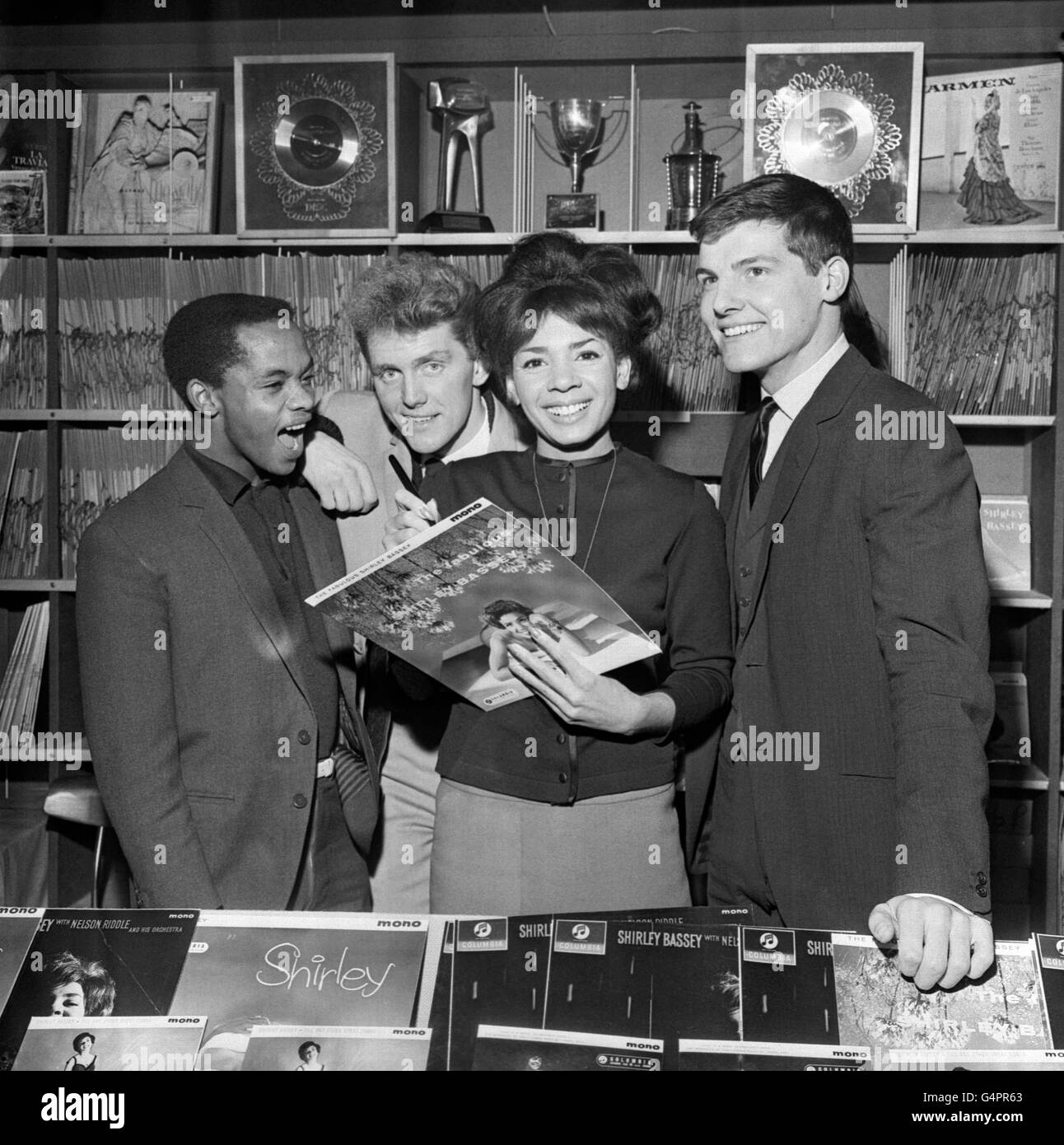 Singing star Shirley Bassey autographs the sleeve of one of her own records at the opening of the Shirley Bassey Record Shop in West End Lane, London. Looking on are pop singers (l-r) Danny Williams, Shane Fenton (later Alvin Stardust) and Jess Conrad. Shirley's record shop is an extension of a bookshop owned by her husband, film producer Kenneth Hume. After finishing her season at the Talk of the Town, Shirley Bassey will leave for New York for a five-week engagement in the Persian Room at the Plaza Hotel. This will be followed by a four-week season in cabaret in Sydney Australia. Stock Photo