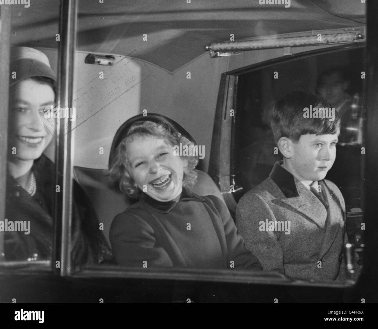 A laughing Princess Anne sits with her mother, Queen Elizabeth II, and Prince Charles in a car taking them from Buckingham Palace to King's Cross Station, London. They were on their way to Sandringham for the Christmas holidays. Stock Photo