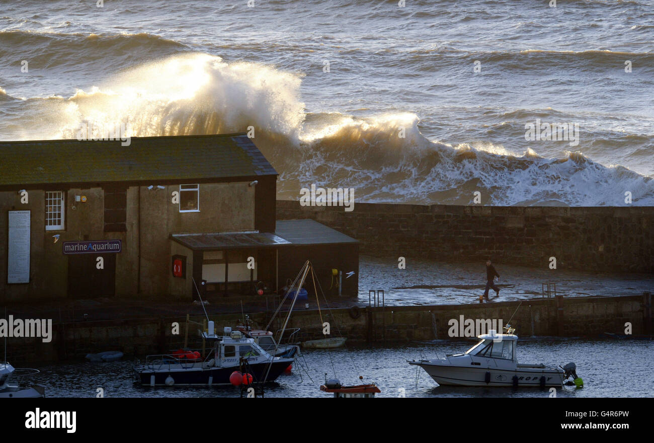 Waves break over the seawall behind houses on the Cobb at Lyme Regis as stormy conditions continued across the UK. Stock Photo
