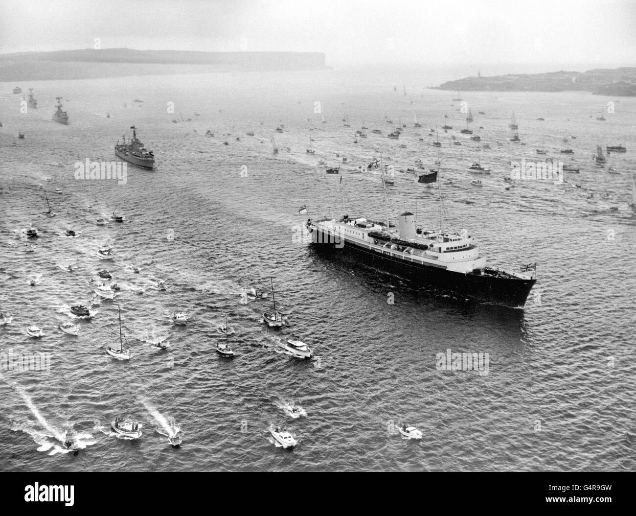 Escorted by an armada of small craft, the Royal Yacht Britannia, bearing Queen Elizabeth II and the Duke of Edinburgh, arrives off Sydney Heads. Three escorting destroyers of the Royal Australian navy follow in her wake. Stock Photo