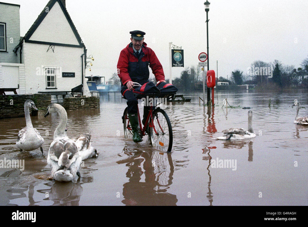 Postman Ray Loveslife-Brown pedals away after delivering to the Swan Hotel at Upton upon Severn. After bursting its banks, water from the nearby river Severn has threatened the hotel for nearly two weeks, forcing closure during the Christmas Period Stock Photo