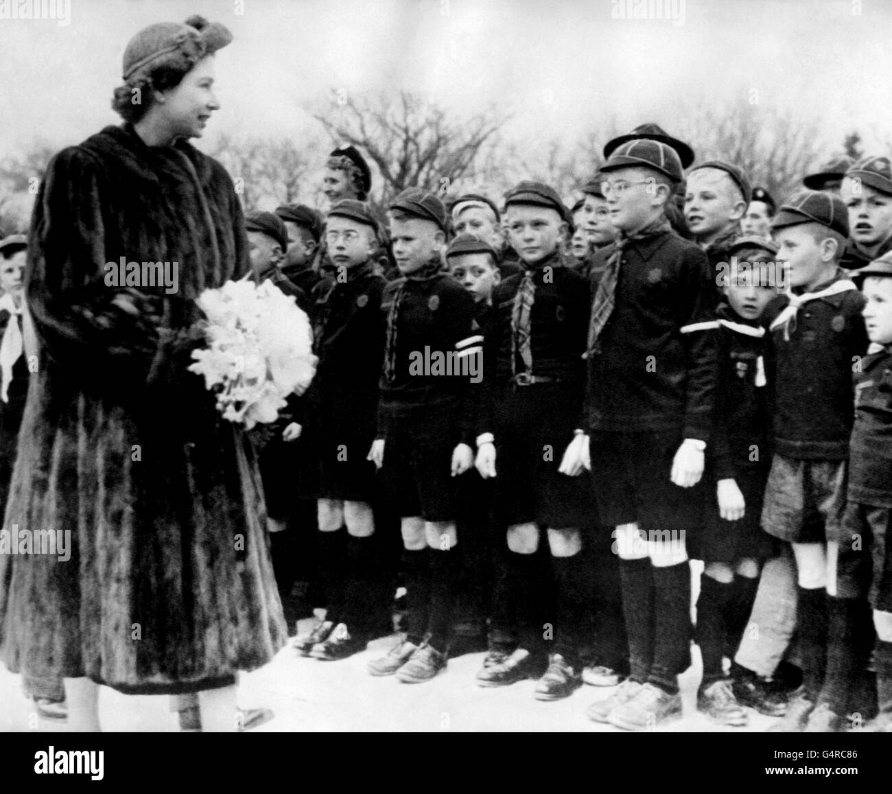 Members of a Canadian 'Wolf Cub Pack,' stand stiffly to attention as the Princess Elizabeth walks by during a casual inspection. The picture was taken in a chilly Regina, Saskatchewan, during the Royal Tour of Canada. Though the weather was cold, and one or two snow flurries occurred, she and the Duke of Edinburgh carried out a full round of engagements. Stock Photo