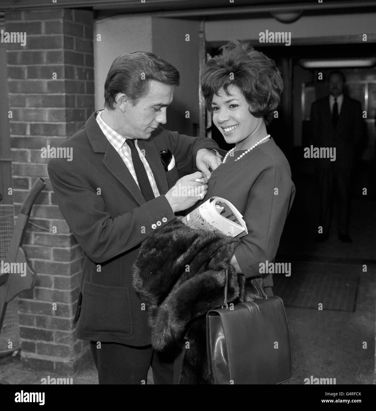 Laden with furs and magazines for the journey, singer Shirley Bassey has her hands full. But her husband, film director Kenneth Hume, is there to manipulate a pin before she boards a BOAC liner at London Airport for New York to fulfil a five week's cabaret engagement. Kenneth Hume was seeing her off. Stock Photo