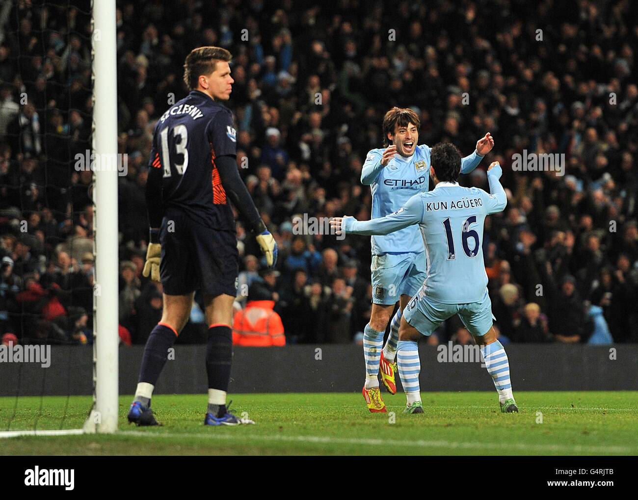 Manchester City's David Silva (centre) celebrates after scoring the first goal with team mate Sergio Aguero (right) as Arsenal goalkeeper Wojciech Szczesny (left) stands dejected Stock Photo