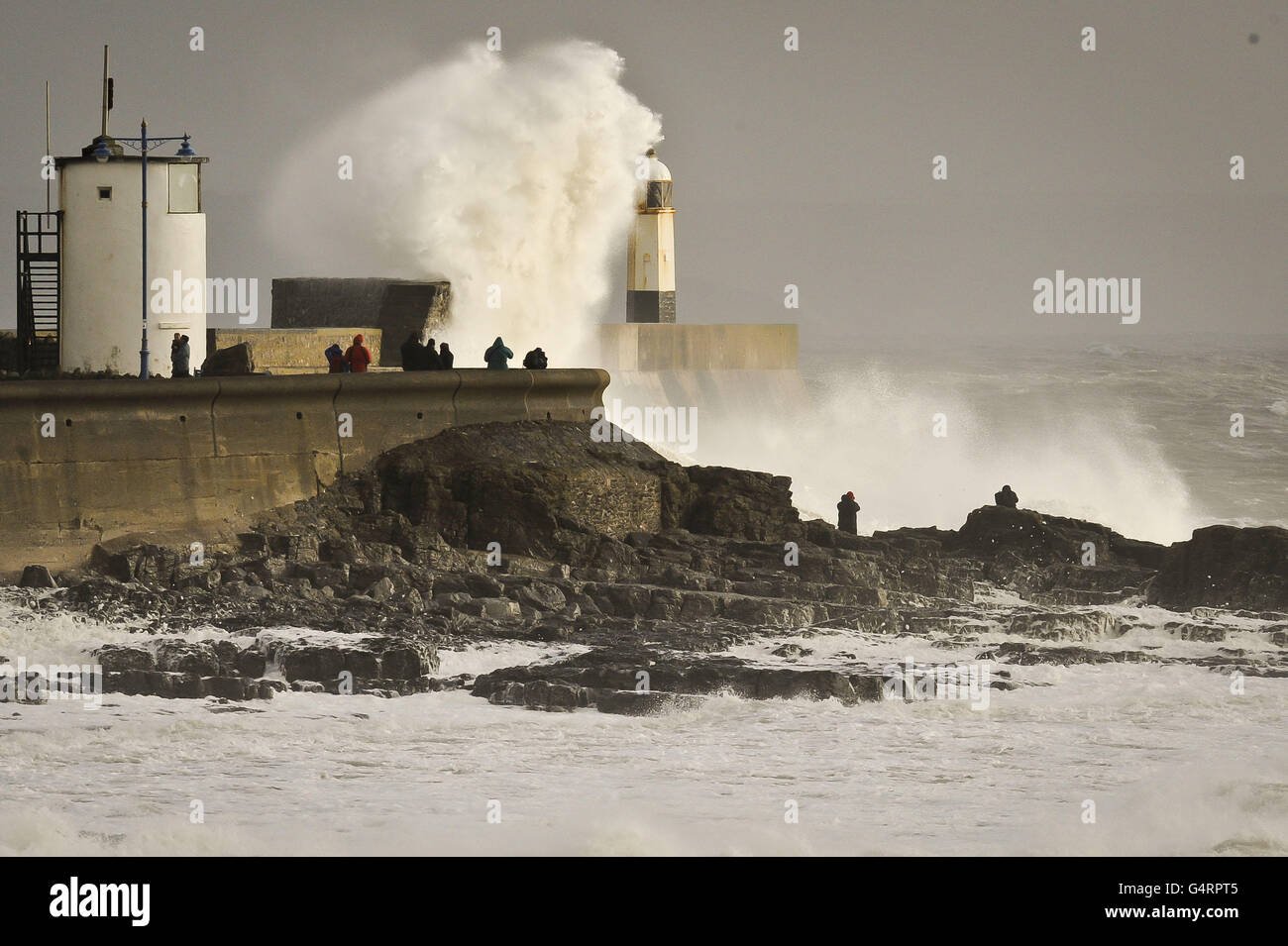 People watch as waves crash against the harbour wall at Porthcawl in South Wales as fierce storms battered Britain today, with heavy rain and winds gusting up to 85mph. Stock Photo