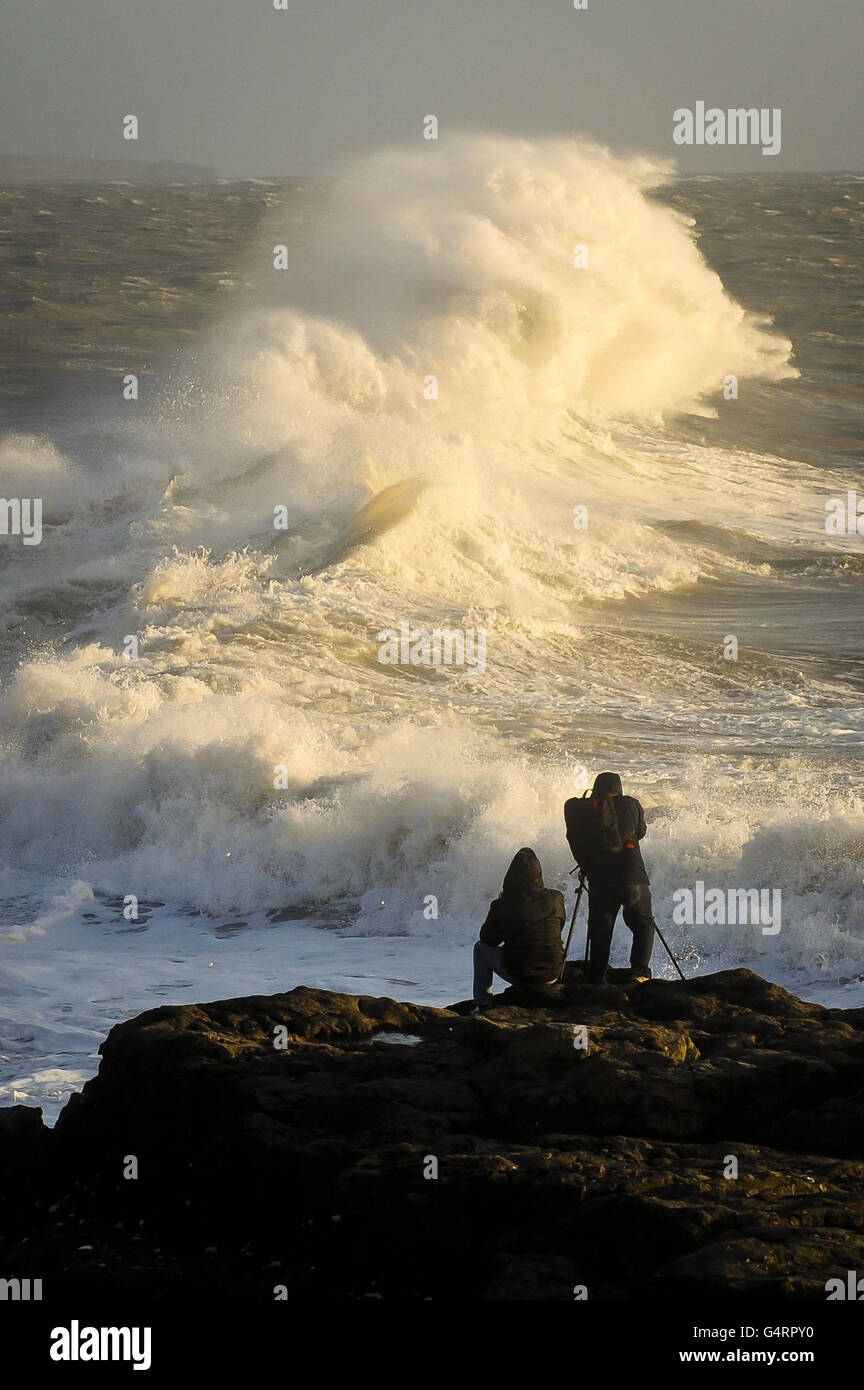 Photographers capture huge waves in the setting sun on the rocks beside the harbour wall at Porthcawl in South Wales as fierce storms battered Britain today, with heavy rain and winds gusting up to 85mph. Stock Photo