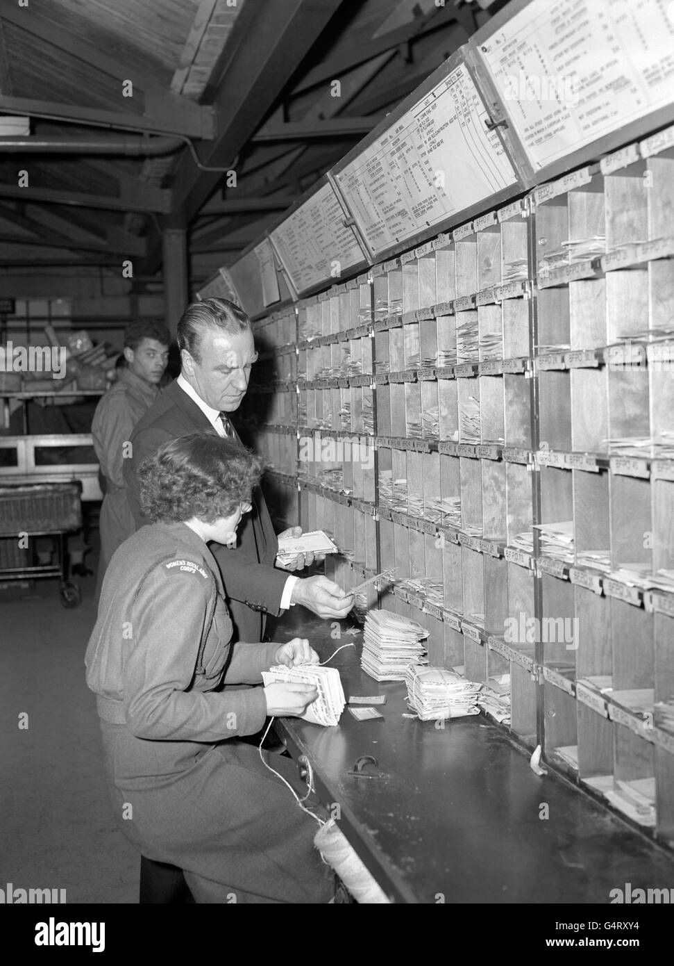 Postmaster General, Ernest Marples, gives a helping hand to Private Isobel Clark as she sorts mail at the Army's Home Postal Depot at North Acton, London. The PMG was visiting the depot to see Christmas mail being sorted for Forces overseas. Stock Photo