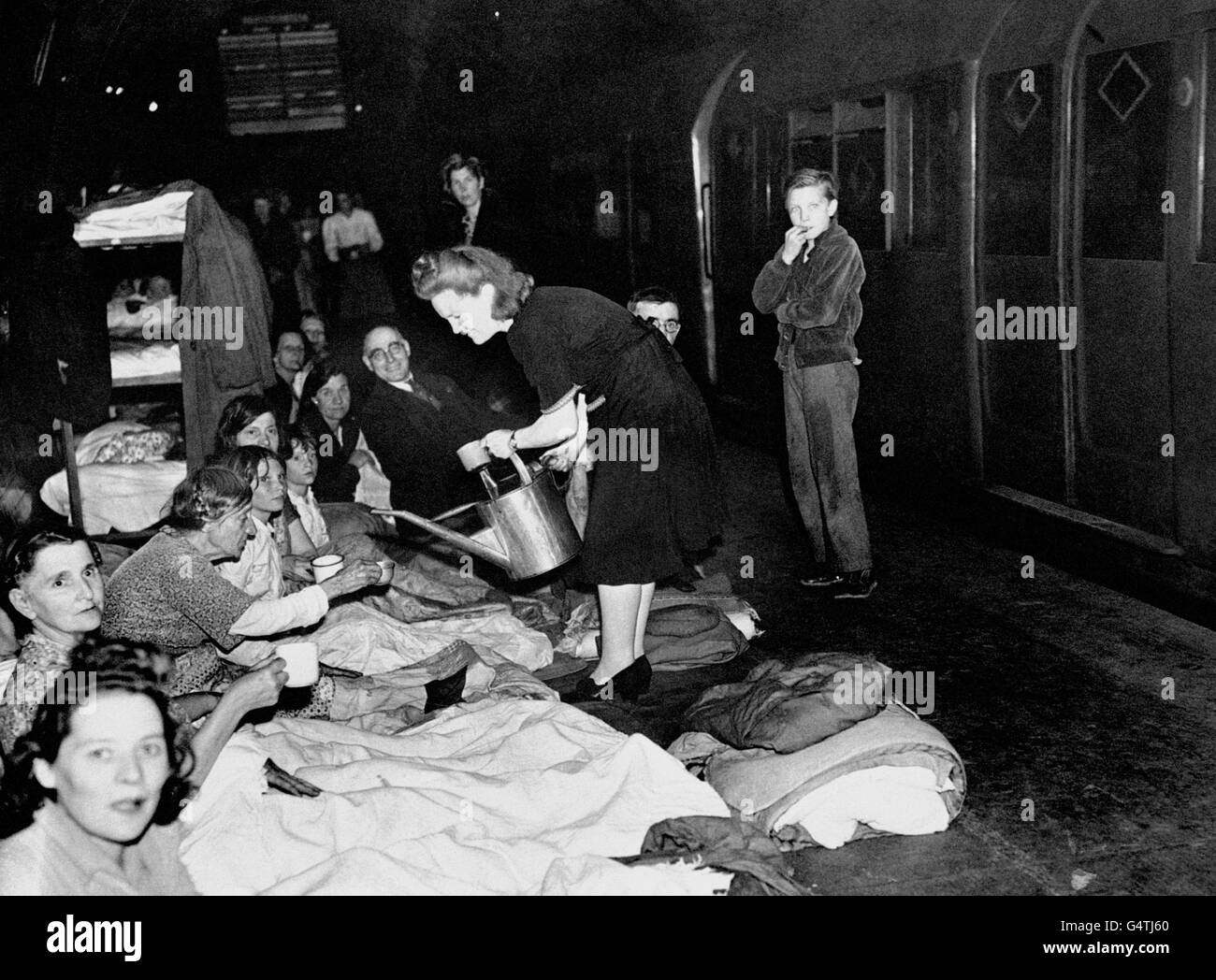 A woman dispenses water from a watering can as Londoners take shelter in the London Underground during the Blitz. Stock Photo