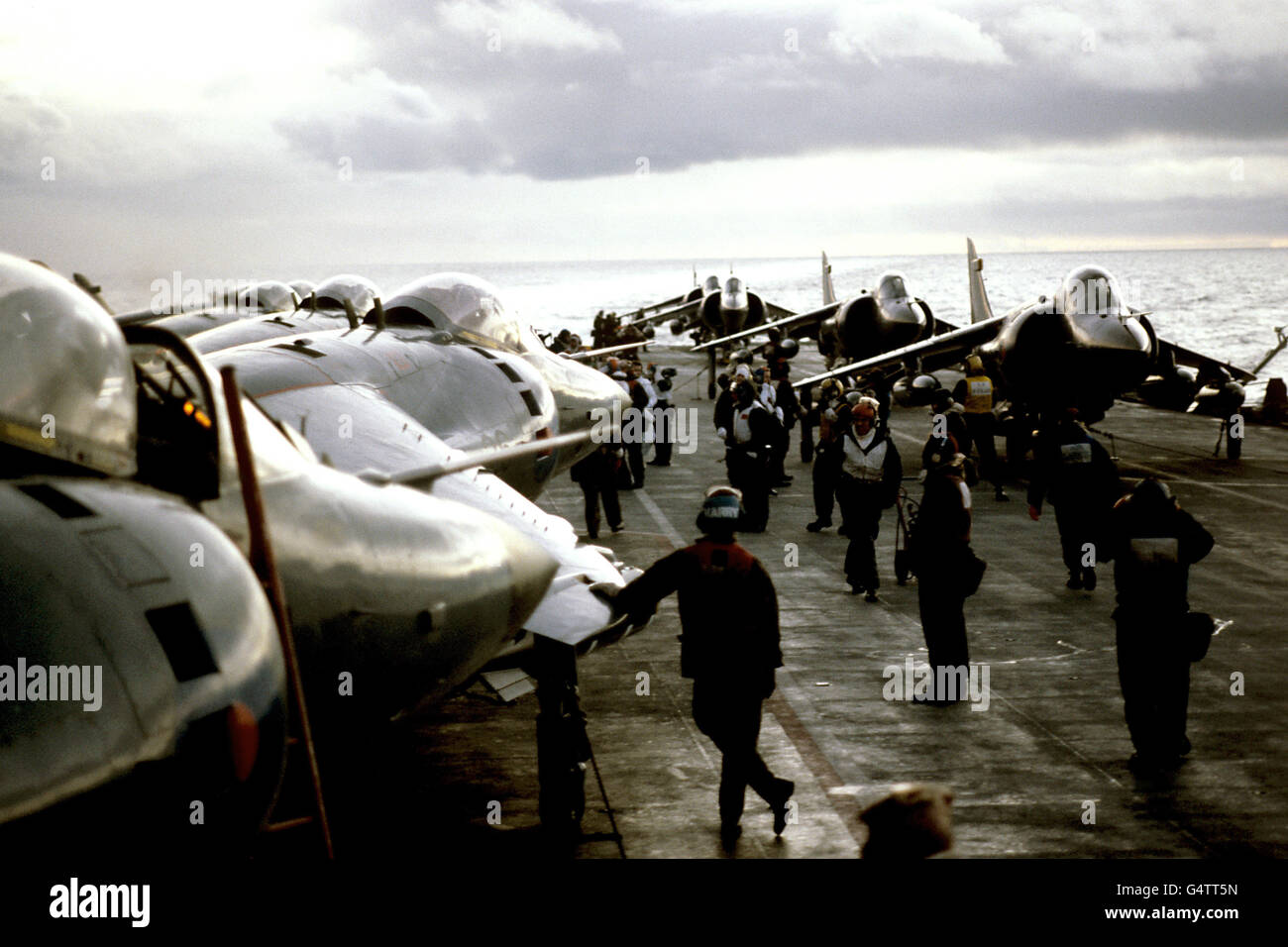 Crewmen swarm around Sea Harriers on the flight deck of the carrier HMS Hermes as she patrols with the British task force off the Falkland Islands. Stock Photo
